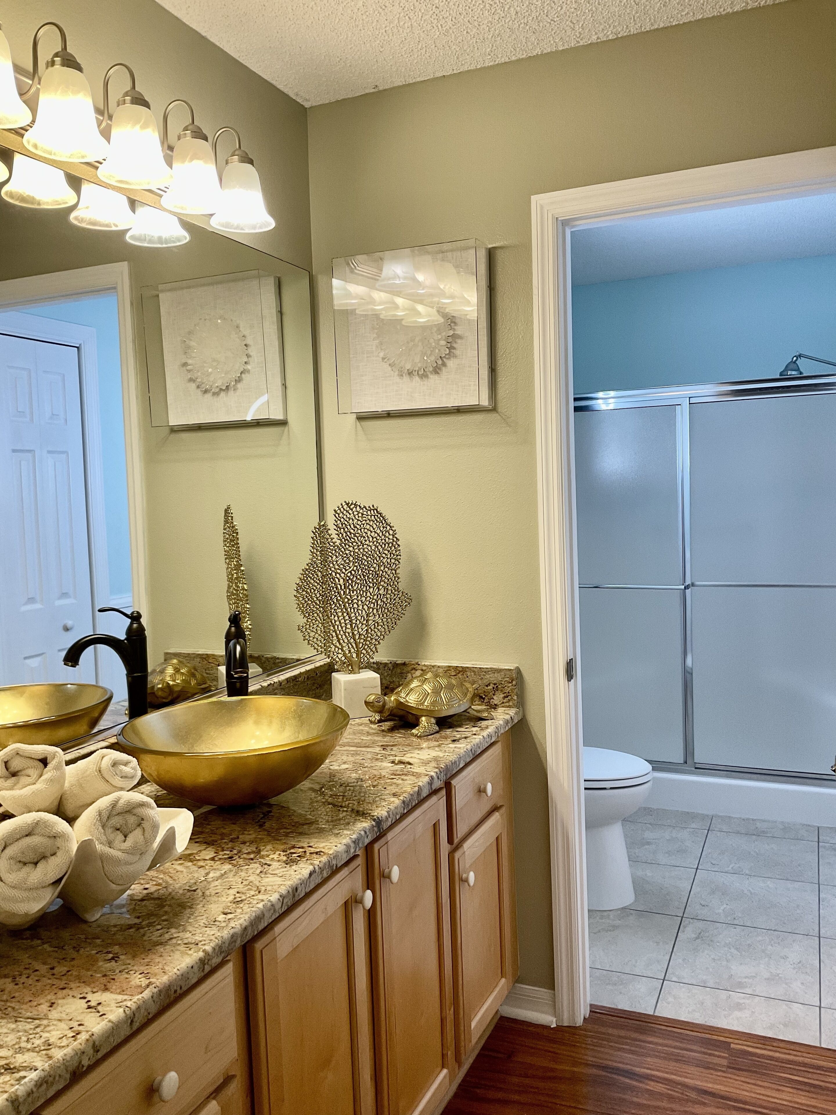 A bathroom with a vanity, a large gold bowl sink, a mirror, and a shower area.