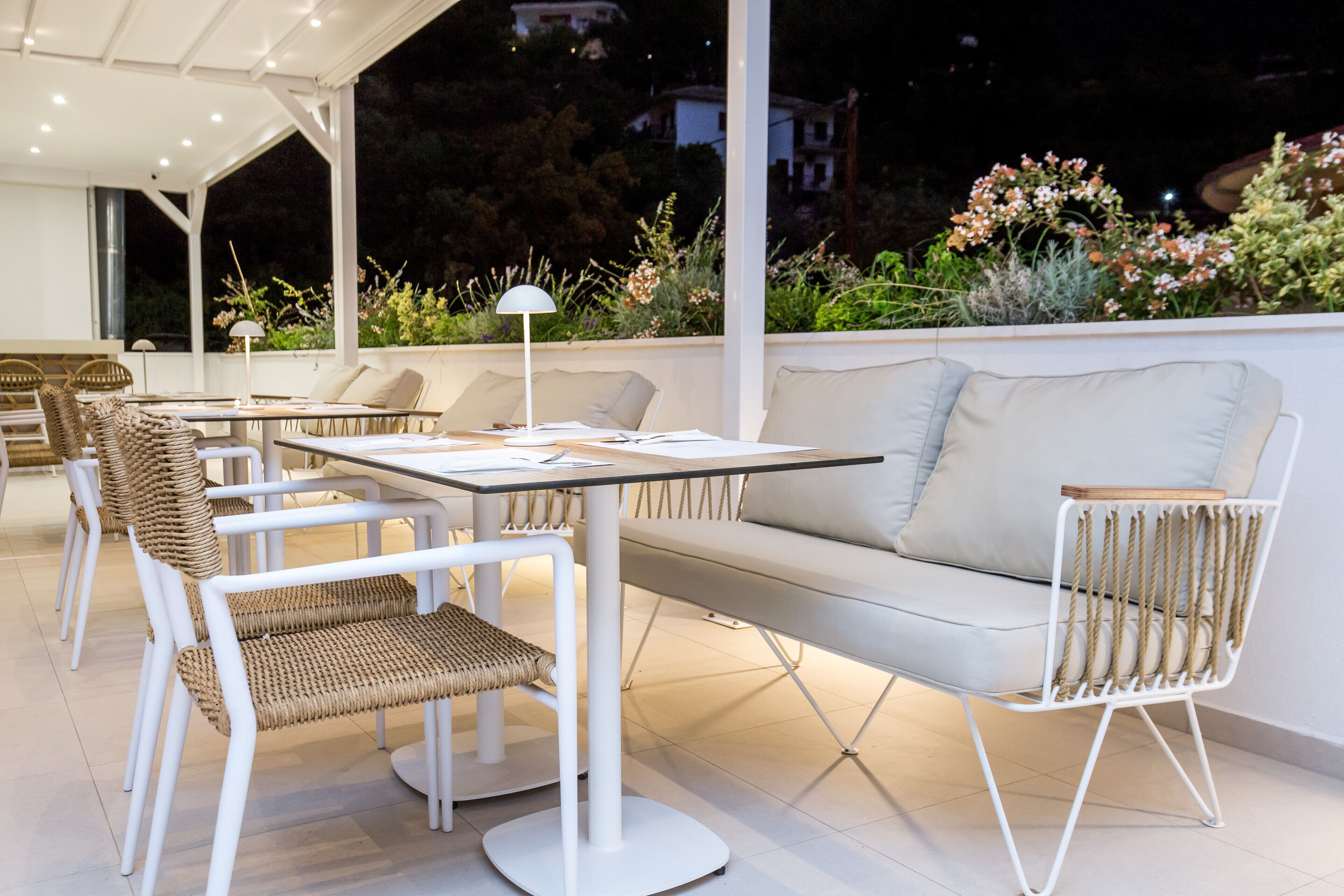An outdoor patio with white furniture, including a sofa and chairs, and a table.