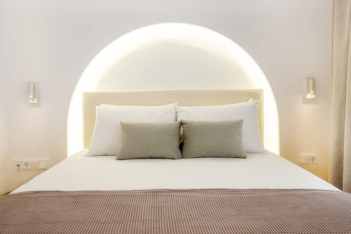 Ein ordentlich bezogenes Bett mit einem Kopfteil, das über dem Bett gebogen ist, zwei Nachttischlampen und eine Steckdose an der Wand.