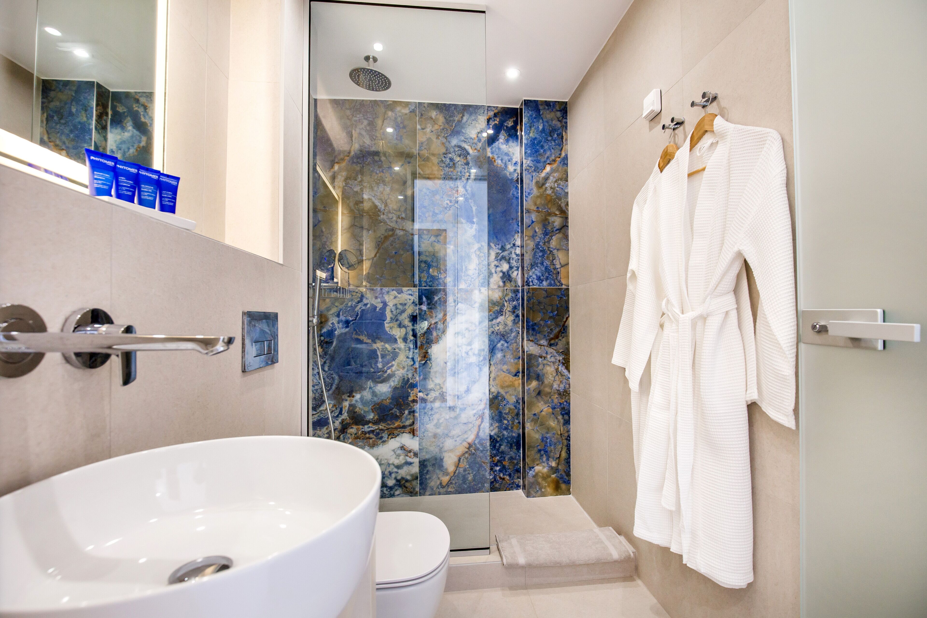 A modern bathroom with a large white sink, a glass shower enclosure, and a robe hanging on a rack.