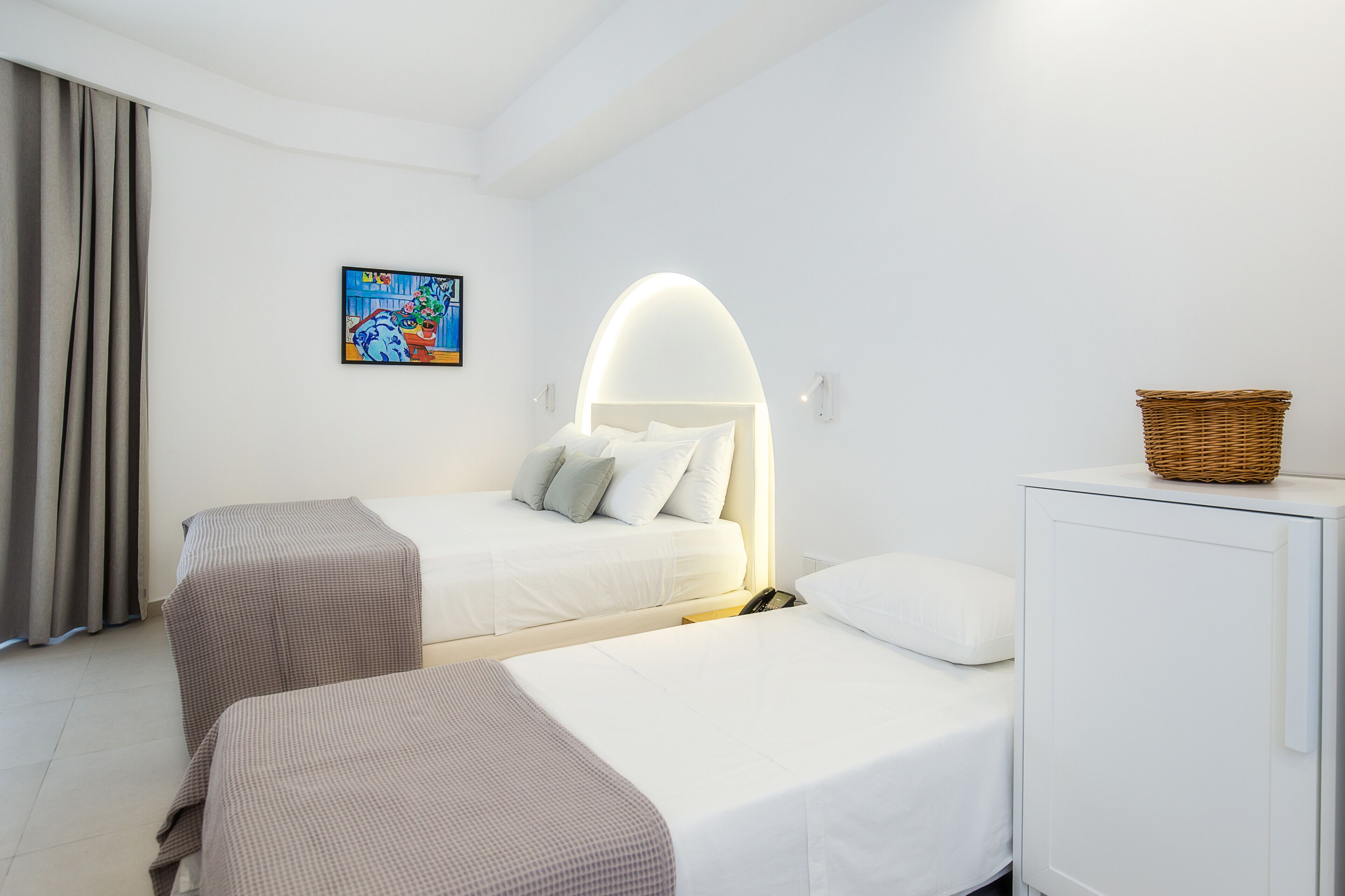 A hotel room with two beds, a white wardrobe, a painting on the wall, and a large window with curtains.
