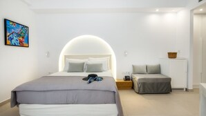 Une chambre moderne avec un grand lit, une table de chevet, un petit canapé et une lampe fixée au mur.