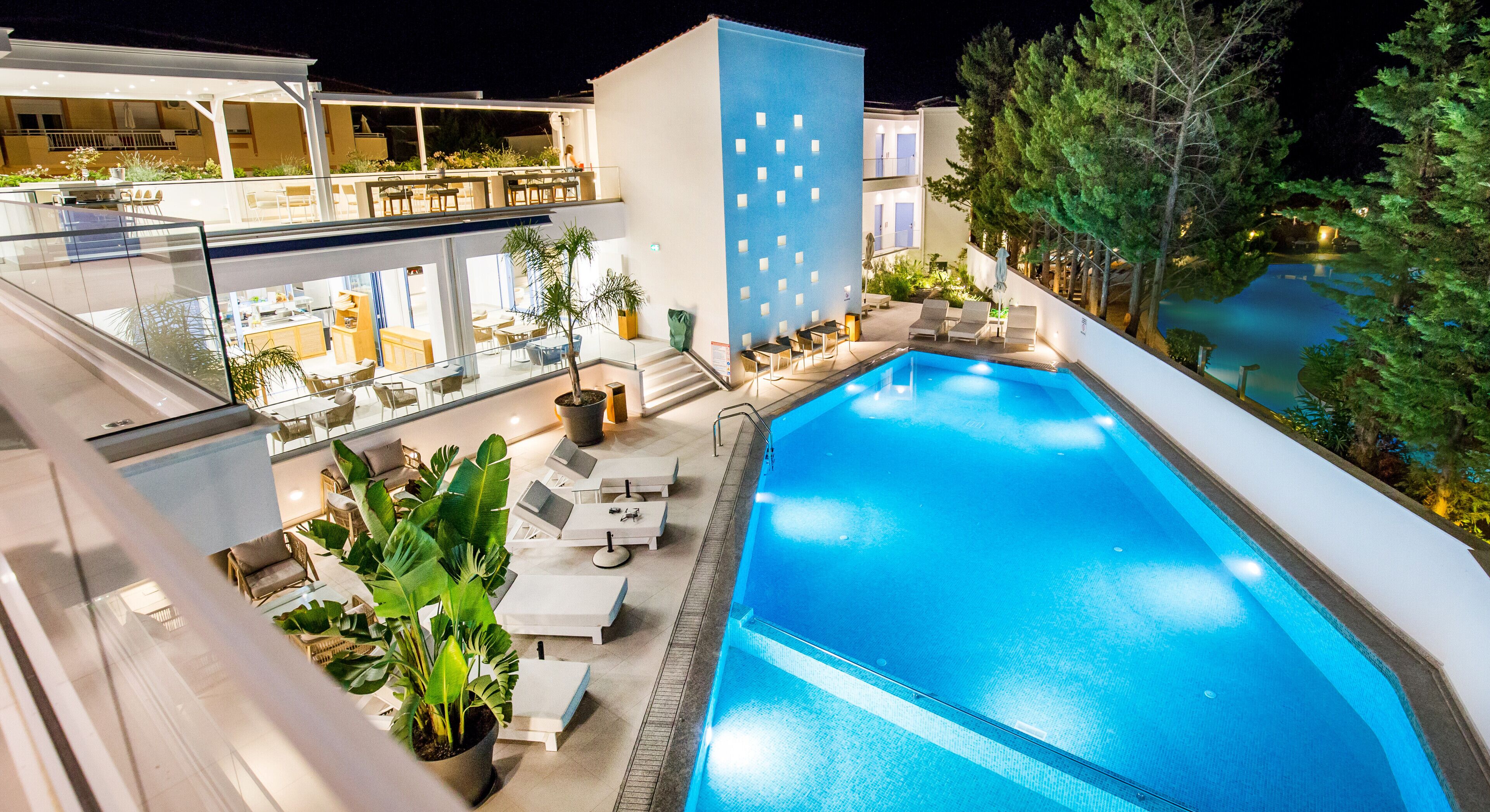 A modern hotel with a rooftop pool, outdoor seating, and lush greenery.