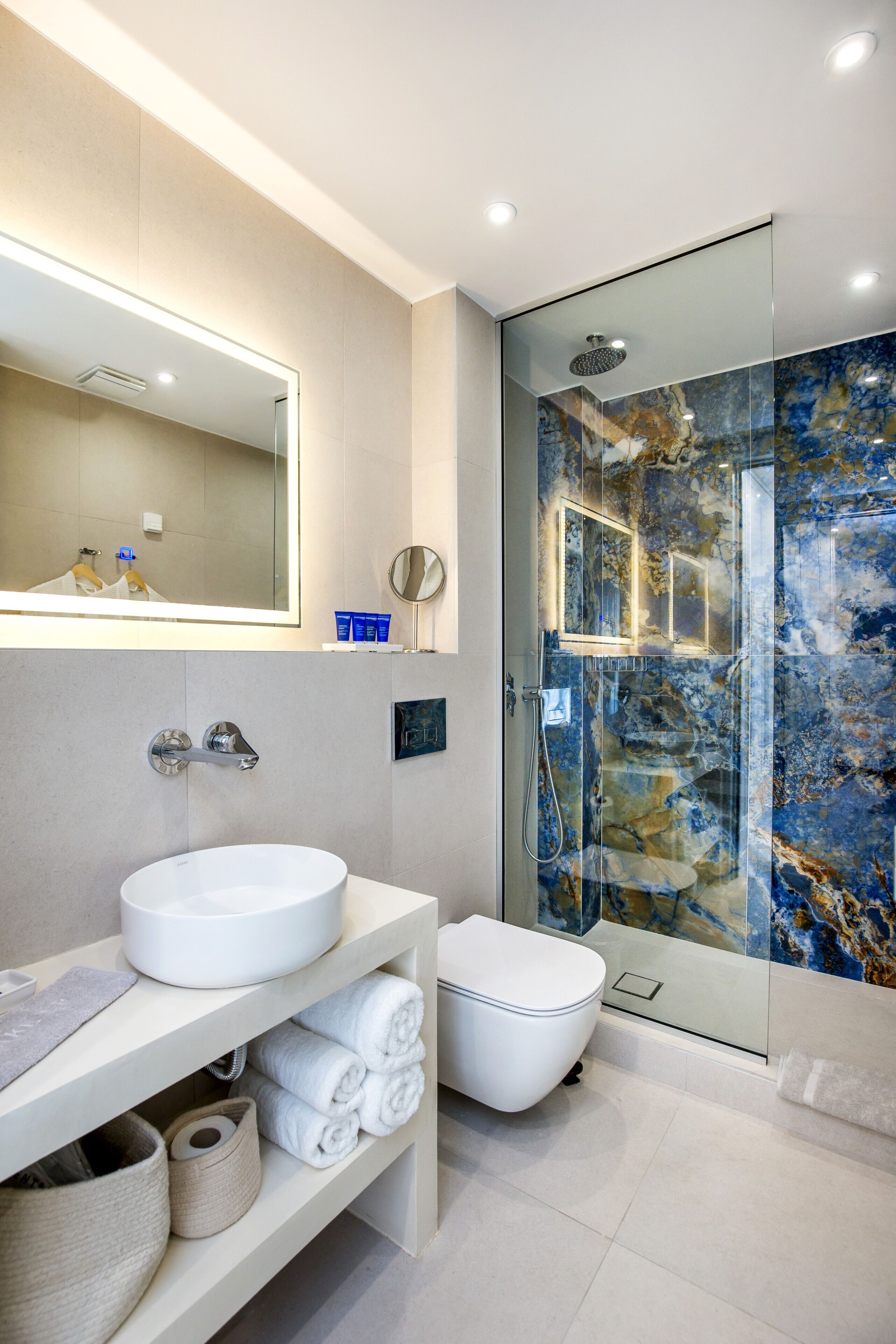 A modern bathroom with a white sink, a glass-enclosed shower, and a marble-tiled wall.