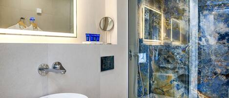 A modern bathroom with a white sink, a glass-enclosed shower, and a marble-tiled wall.