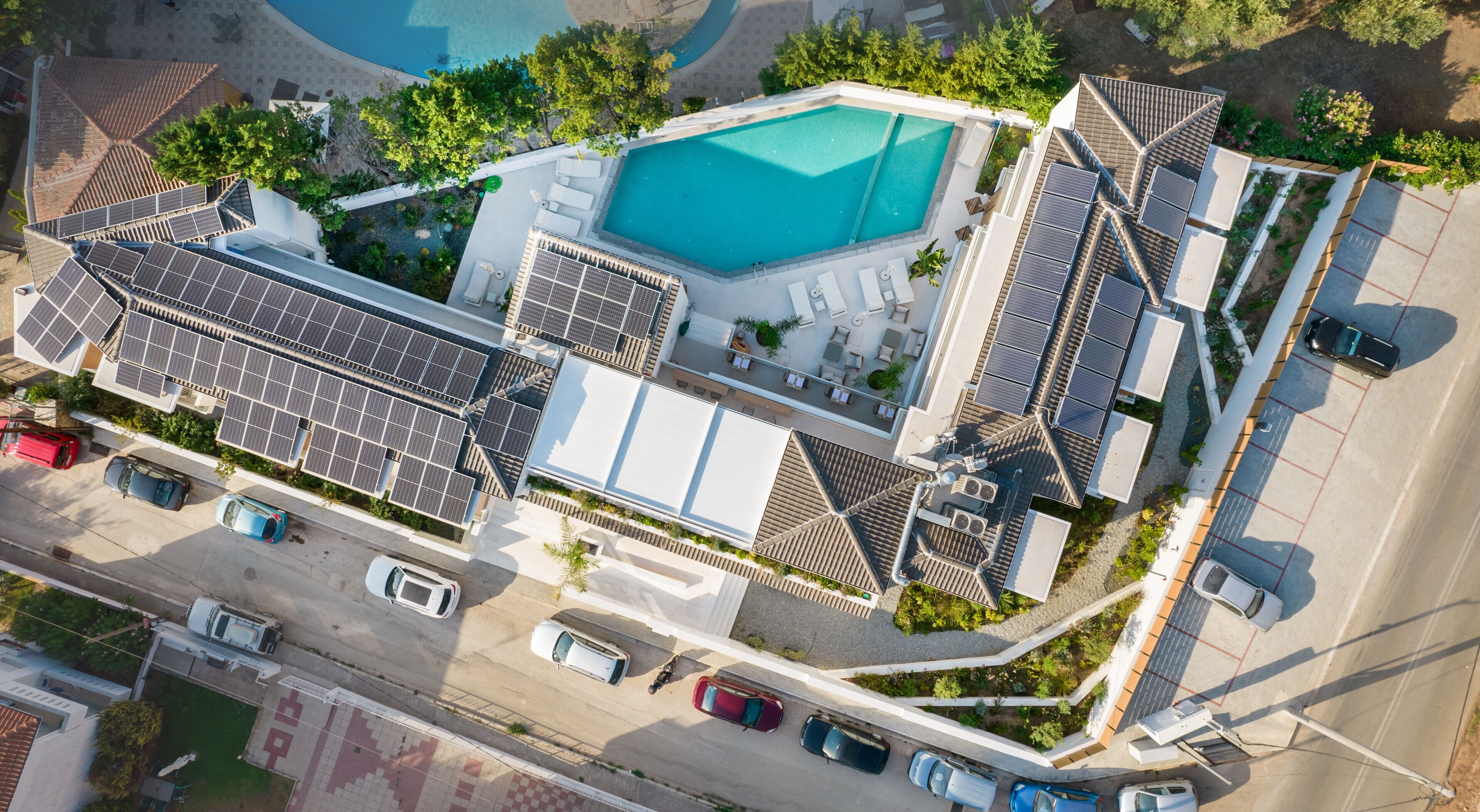 An aerial view of a residential property with a swimming pool, solar panels, and a parking area.