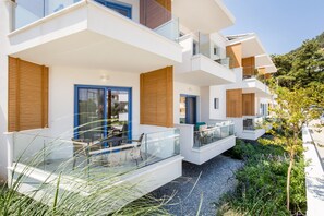 Um edifício residencial moderno de vários andares, com varandas, entrada com calçada de cascalho e área de jardim.