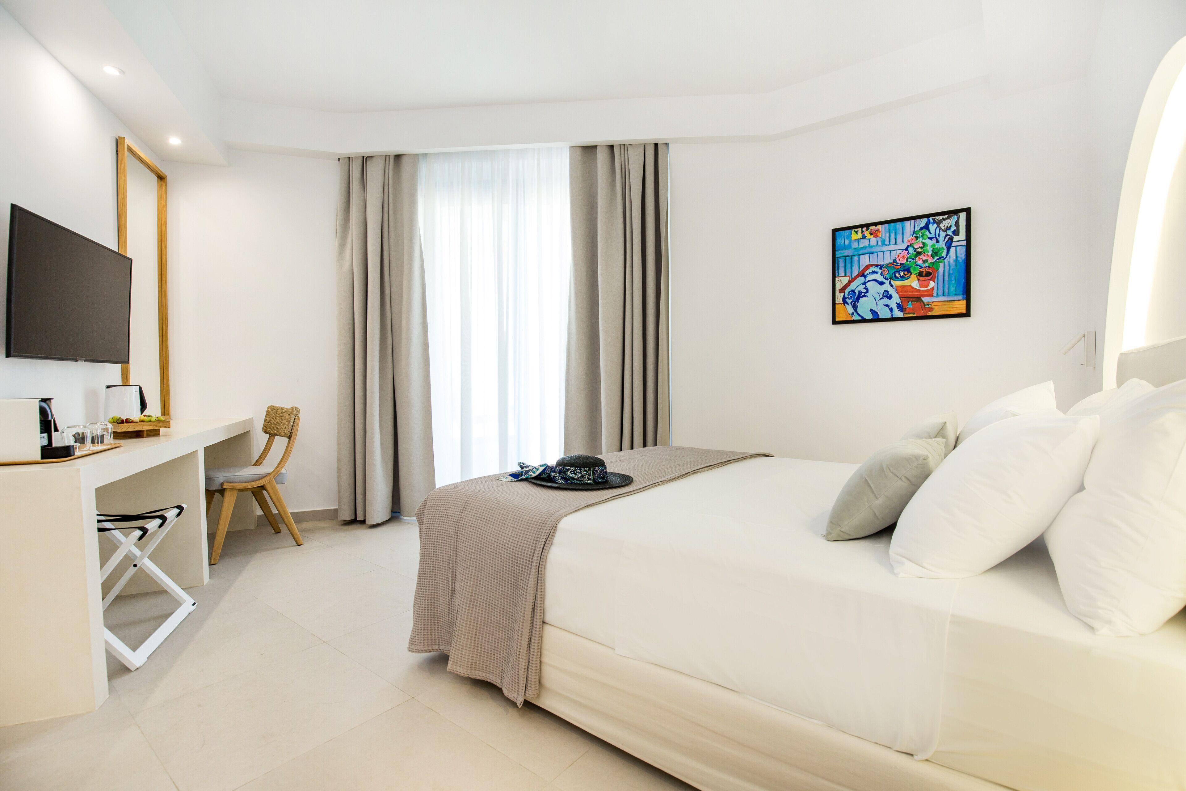 Habitación de hotel con cama, escritorio, silla, televisor y un cuadro en la pared.