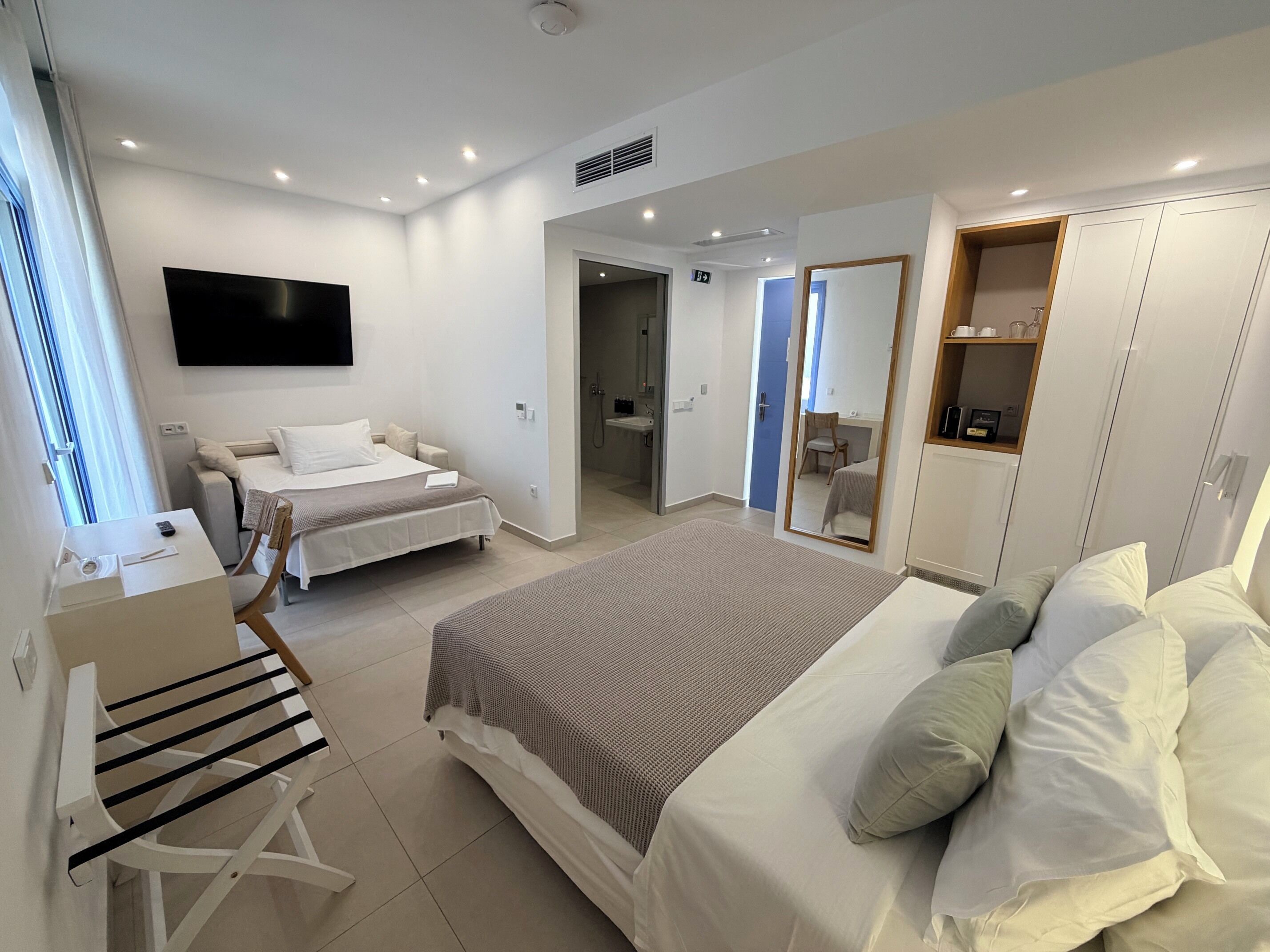 A modern hotel room with a bed, a desk, a chair, a TV, and a wardrobe.