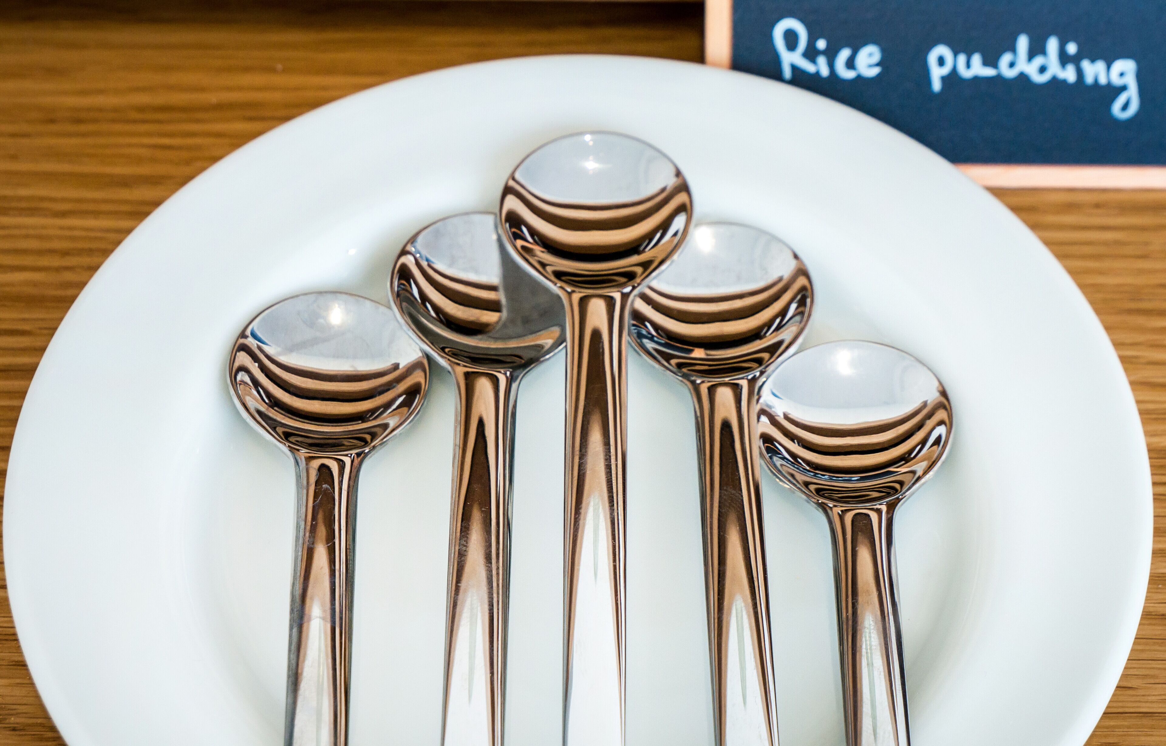 A white plate with five stainless steel spoons on it.