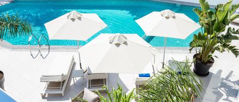 A pool area with white umbrellas, lounge chairs, and potted plants.