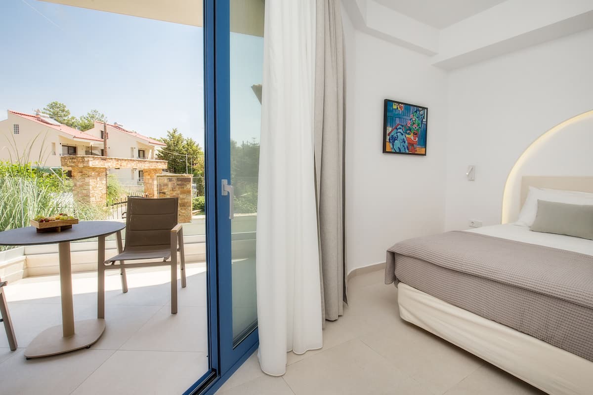 Ein Hotelzimmer mit Bett, Tisch mit Stühlen, einem Balkon mit Blick auf Gebäude und einem Bild an der Wand.