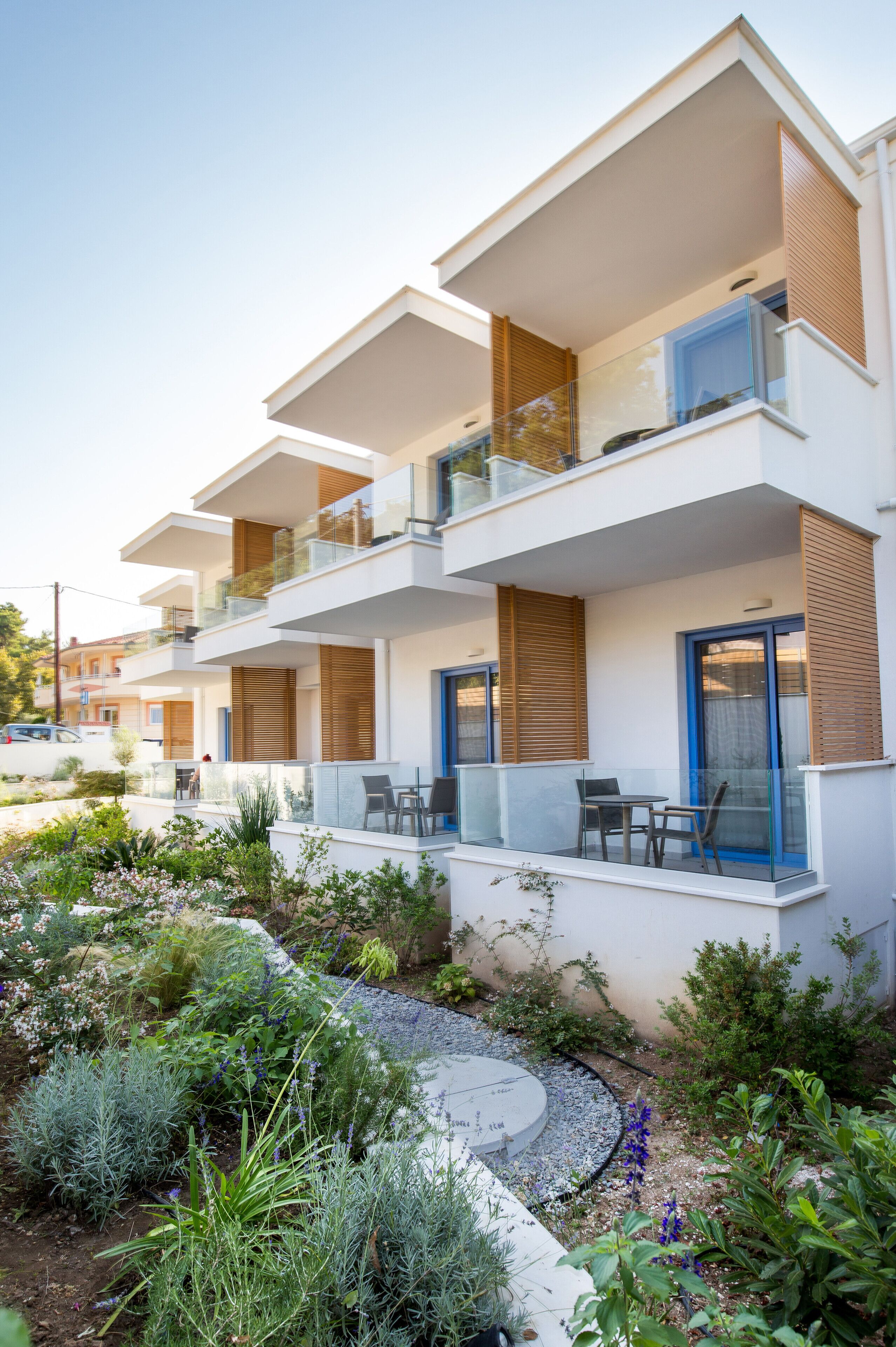 Un immeuble moderne à plusieurs étages, doté de balcons, d’un espace extérieur aménagé pour s’asseoir et d’un jardin paysager.