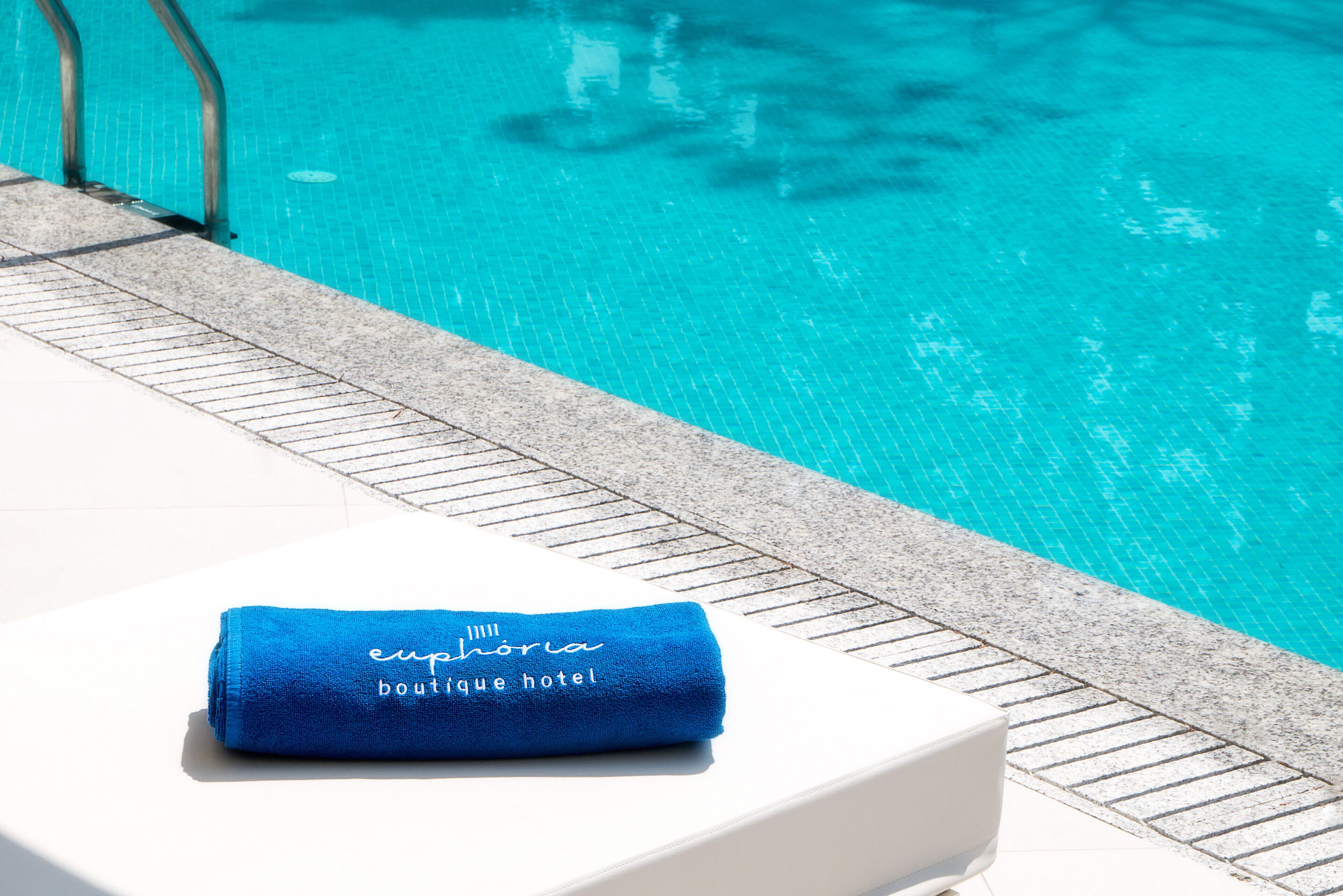 Una toalla azul con la inscripción "euphoría boutique hotel" sobre una superficie blanca cerca de una piscina.