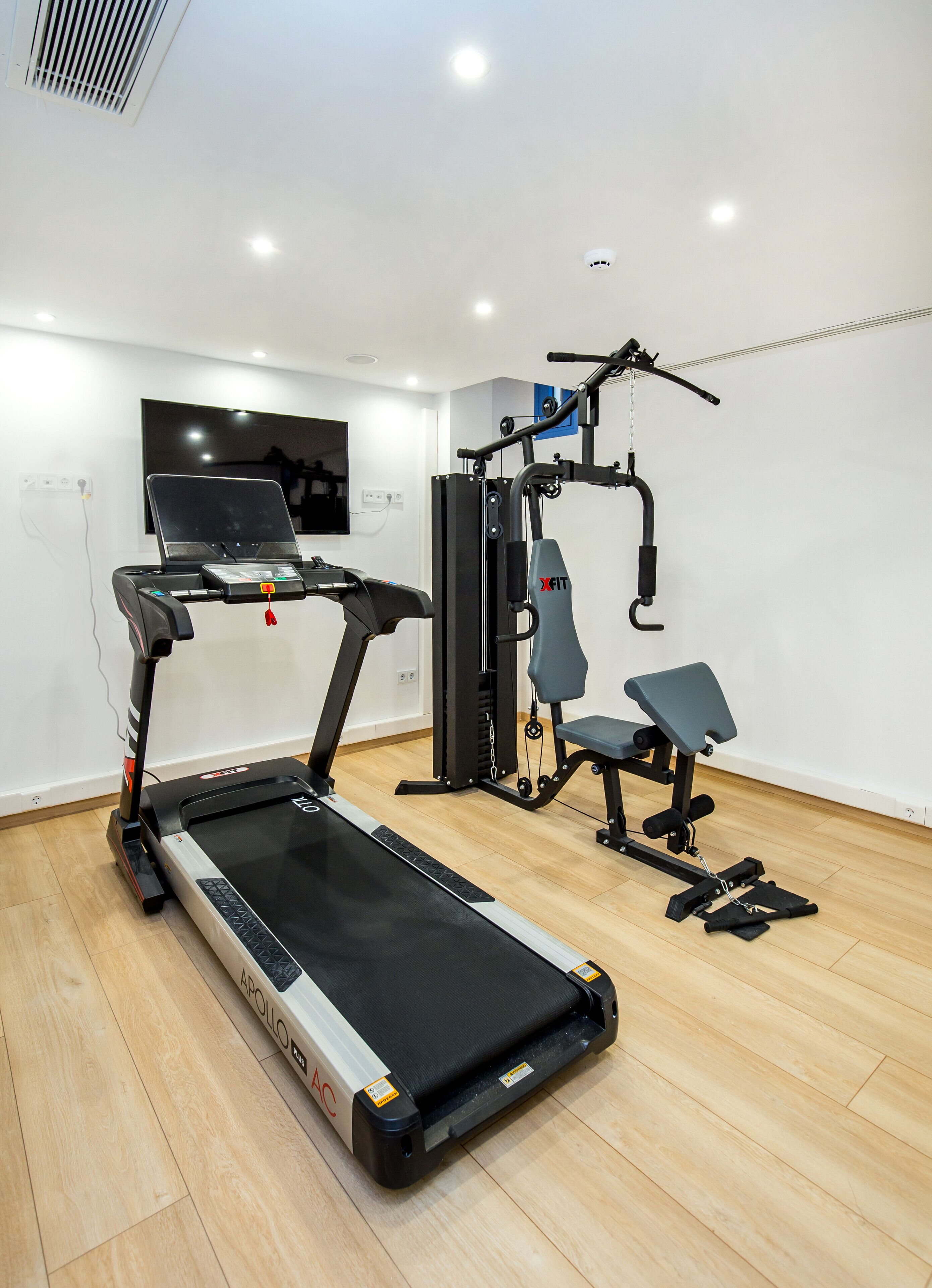 Un gimnasio con cinta de correr, máquina de pesas y banco.