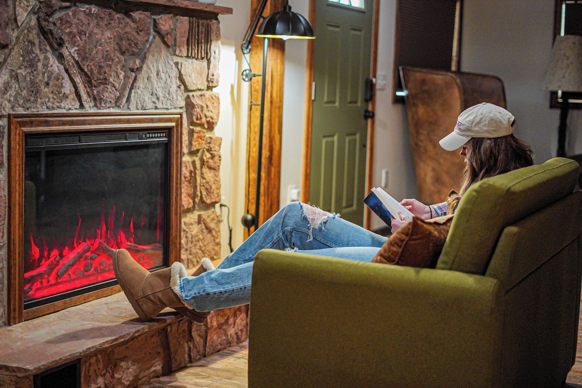 A person sitting on a green armchair in front of a fireplace with a stone wall and a wooden door in the background.