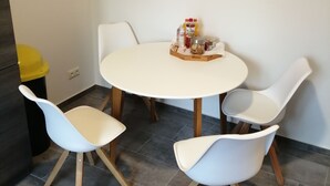 A round dining table with four white chairs, a yellow trash bin, and a small table with condiments. - Komfortable Ferienwohnung mit Parklplatz (Zossen)