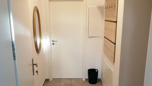 A hallway with a white door, a trash bin, and a wooden shelf unit. - Komfortable Ferienwohnung mit Parklplatz (Zossen)