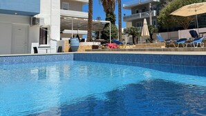 A swimming pool with clear blue water, surrounded by palm trees and lounge chairs. - Simple Hotel Hersonissos Blue (Hersonissos)