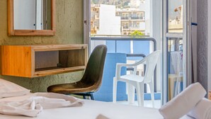 A hotel room with a bed, a chair, a small table, a mirror, and a view of a mountain. - Simple Hotel Hersonissos Blue (Hersonissos)