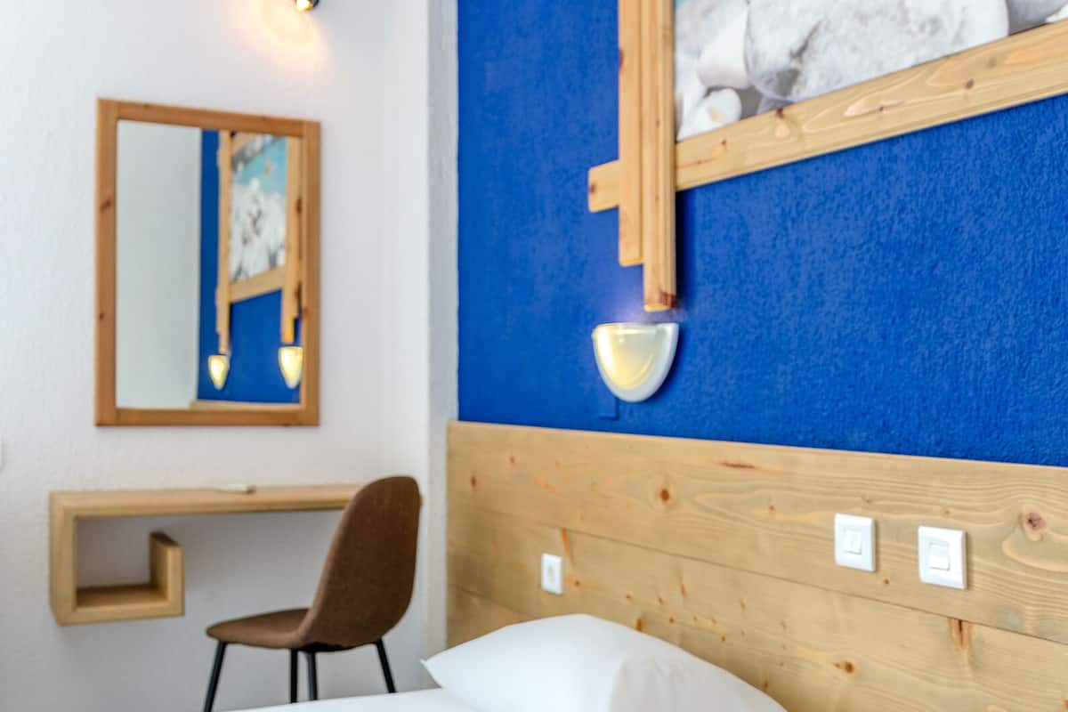 A hotel room with a wooden headboard, a desk with a chair, a large mirror, and a painting of rocks on the wall.