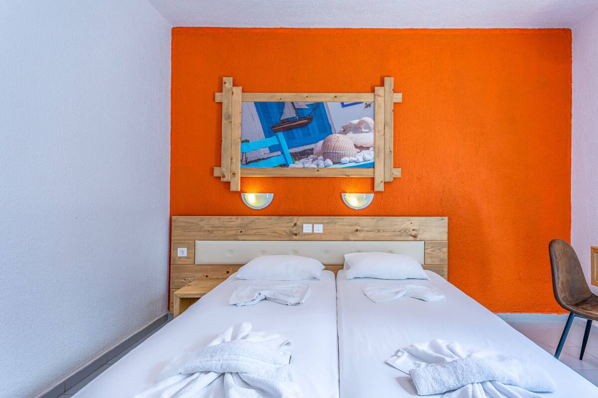 A hotel room with two beds, a wooden headboard, an orange wall, and a framed picture above the beds.