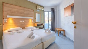 A double bed with white linens and towels, a wooden headboard, a bedside table, a chair, and a view of the outside through a glass door. - Simple Hotel Hersonissos Blue (Hersonissos)