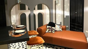 A modern room with a dining table set for two, a sofa with decorative pillows, and a patterned floor. - Trstevere Boutique Suite Roma with Turkish bath (Roma)