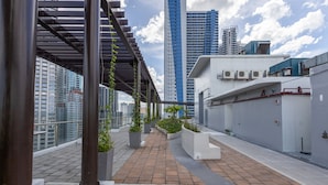 Une terrasse sur le toit, dotée d’une passerelle couverte, de plantes en pot et offrant une vue sur les grands immeubles.