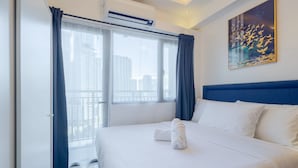 Une chambre d’hôtel avec un grand lit, une fenêtre avec des rideaux, un appareil de climatisation et un tableau au mur.