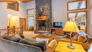 A cozy living room with a stone fireplace, leather sofas, a coffee table, and a television. - Gorgeous Renovated Home With Mirror Lake Access! (Lake Placid)