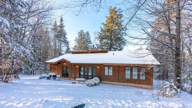 A wooden cabin with a snow-covered roof, surrounded by trees and a snowy landscape. - Gorgeous Renovated Home With Mirror Lake Access! (Lake Placid)