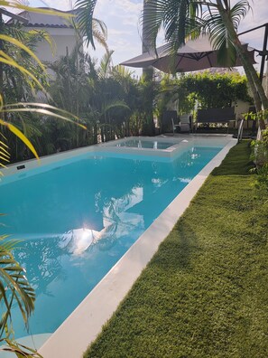 A rectangular swimming pool with clear blue water, surrounded by well-maintained grass and palm trees. - Beautiful Villa For 20 - Albatros Vacational House On FB (Puerto Vallarta)