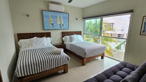 Habitación de hotel con dos camas, un ventanal con vista a palmeras y obras de arte en las paredes.