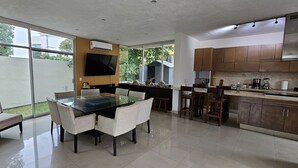 Una cocina moderna con una isla grande, un comedor con mesa de vidrio y un televisor montado en la pared.