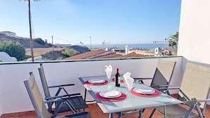 Mesa posta para dois numa varanda, com vista ampla para o mar e edifícios ao longe.