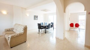 Ampla sala de estar com sofá, mesa de jantar com cadeiras e cozinha com cadeiras vermelhas.