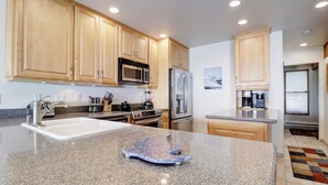 A modern kitchen with granite countertops, stainless steel appliances, wooden cabinets, and a central island. - Ski in Ski out, Amazing Views Condo in East Village VP211 (Copper Mountain)