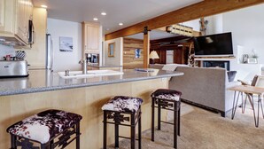 A modern kitchen with a central island, wooden bar stools, and a flat-screen TV mounted on the wall. - Ski in Ski out, Amazing Views Condo in East Village VP211 (Copper Mountain)
