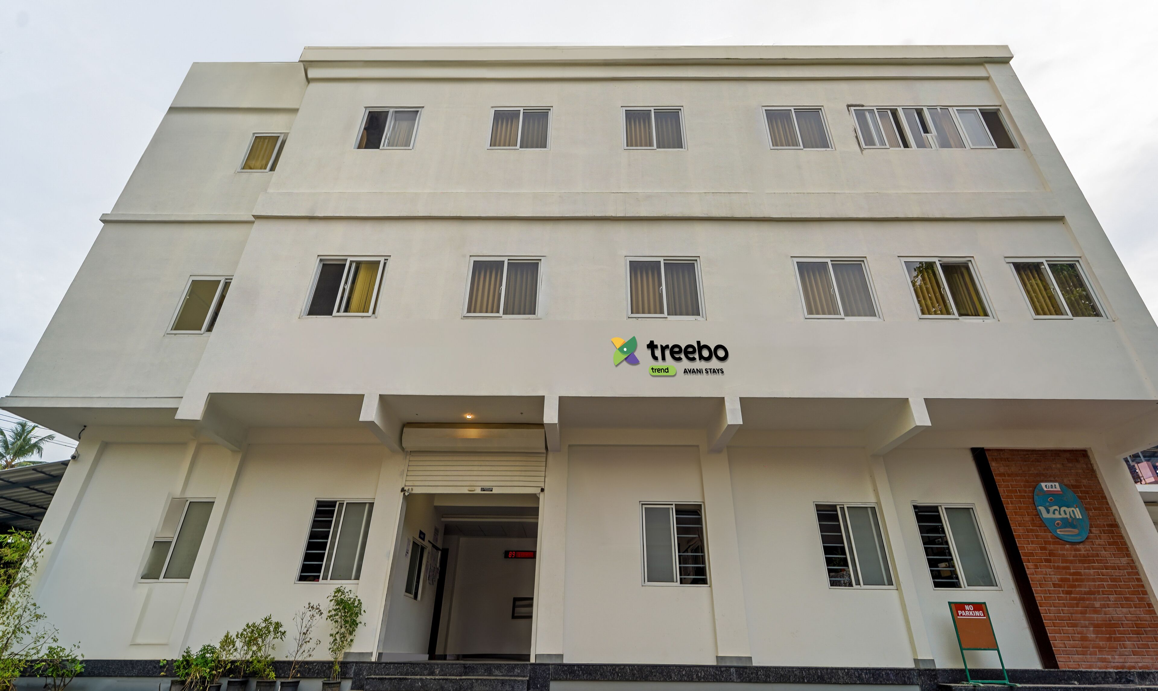 Un edificio de varios pisos con fachada plana, múltiples ventanas y un letrero que dice 'treebo trend AANI STAYS'.