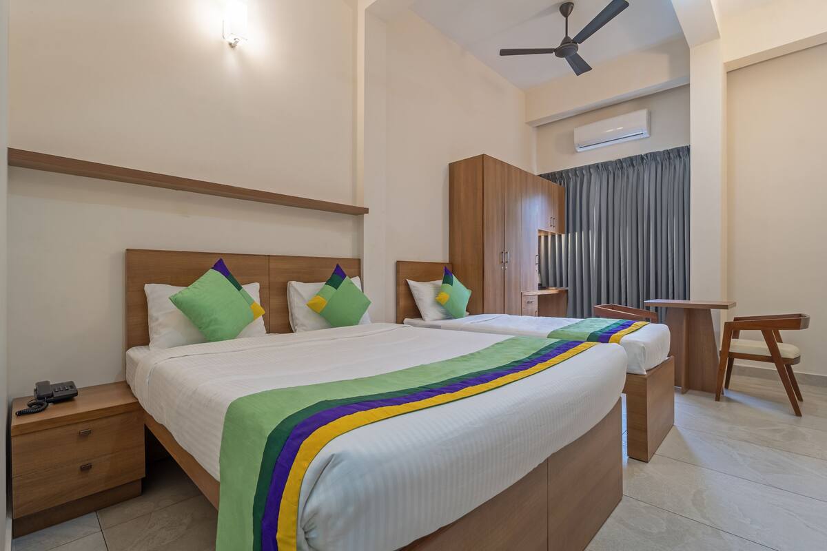 A hotel room with two beds, a desk, a chair, a wardrobe, and a ceiling fan.