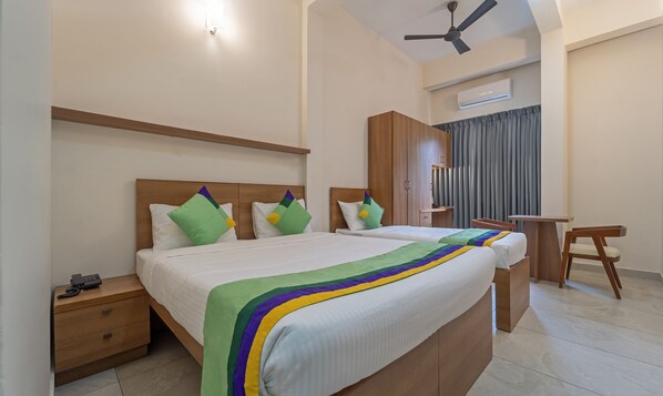 A hotel room with two beds, a desk, a chair, a wardrobe, and a ceiling fan.