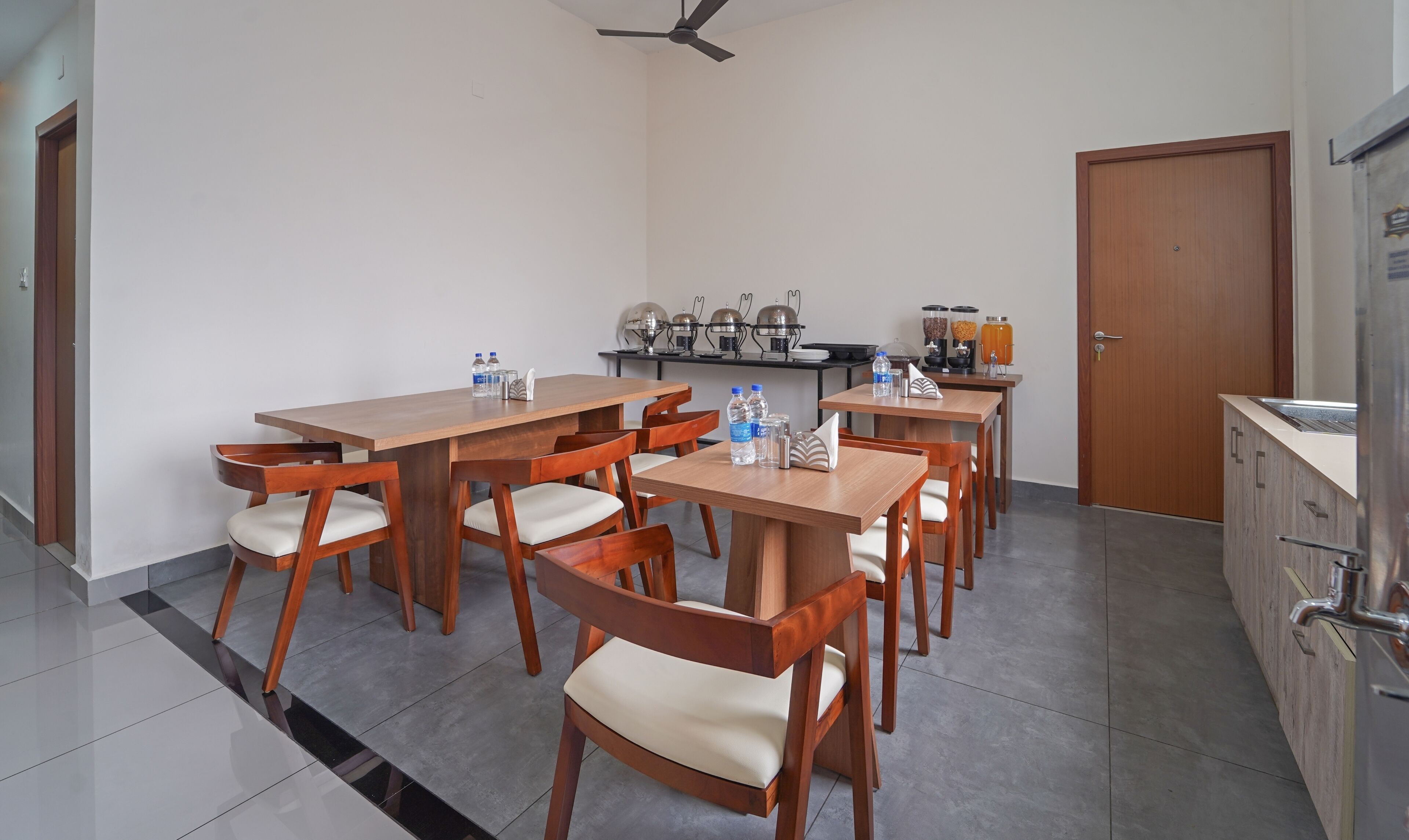 A modern kitchen with wooden tables and chairs, a coffee machine, and a refrigerator.