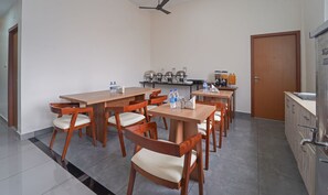 A modern kitchen with wooden tables and chairs, a coffee machine, and a refrigerator.