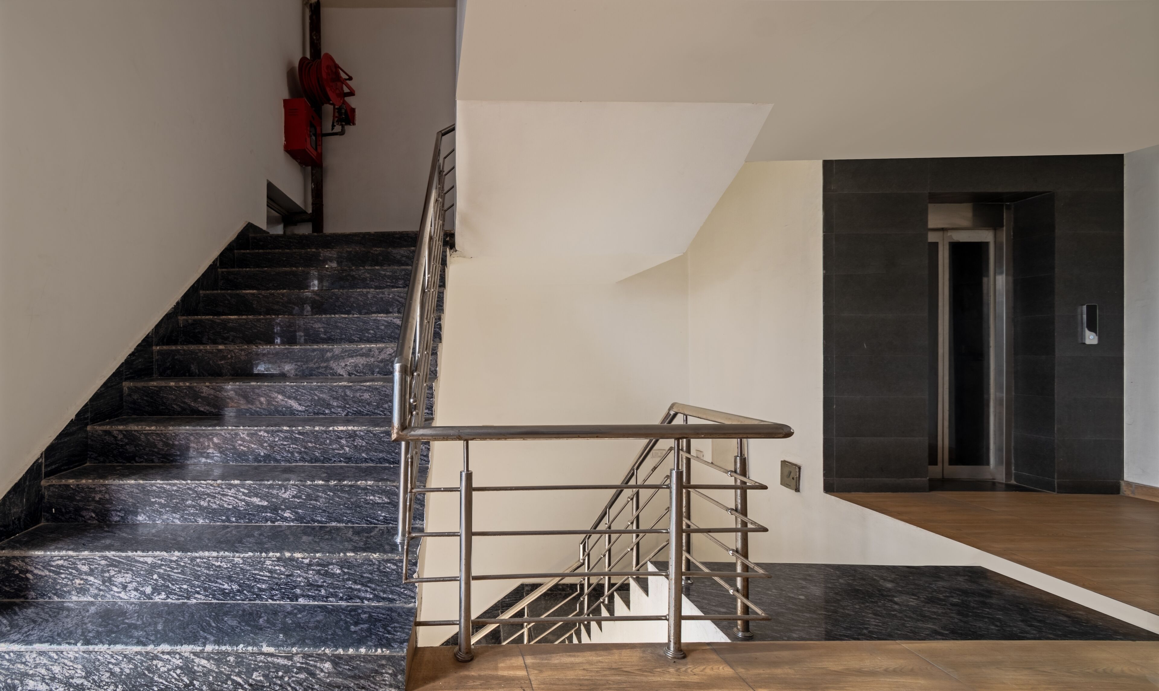 A staircase with black marble steps, a metal handrail, and a wooden floor landing.