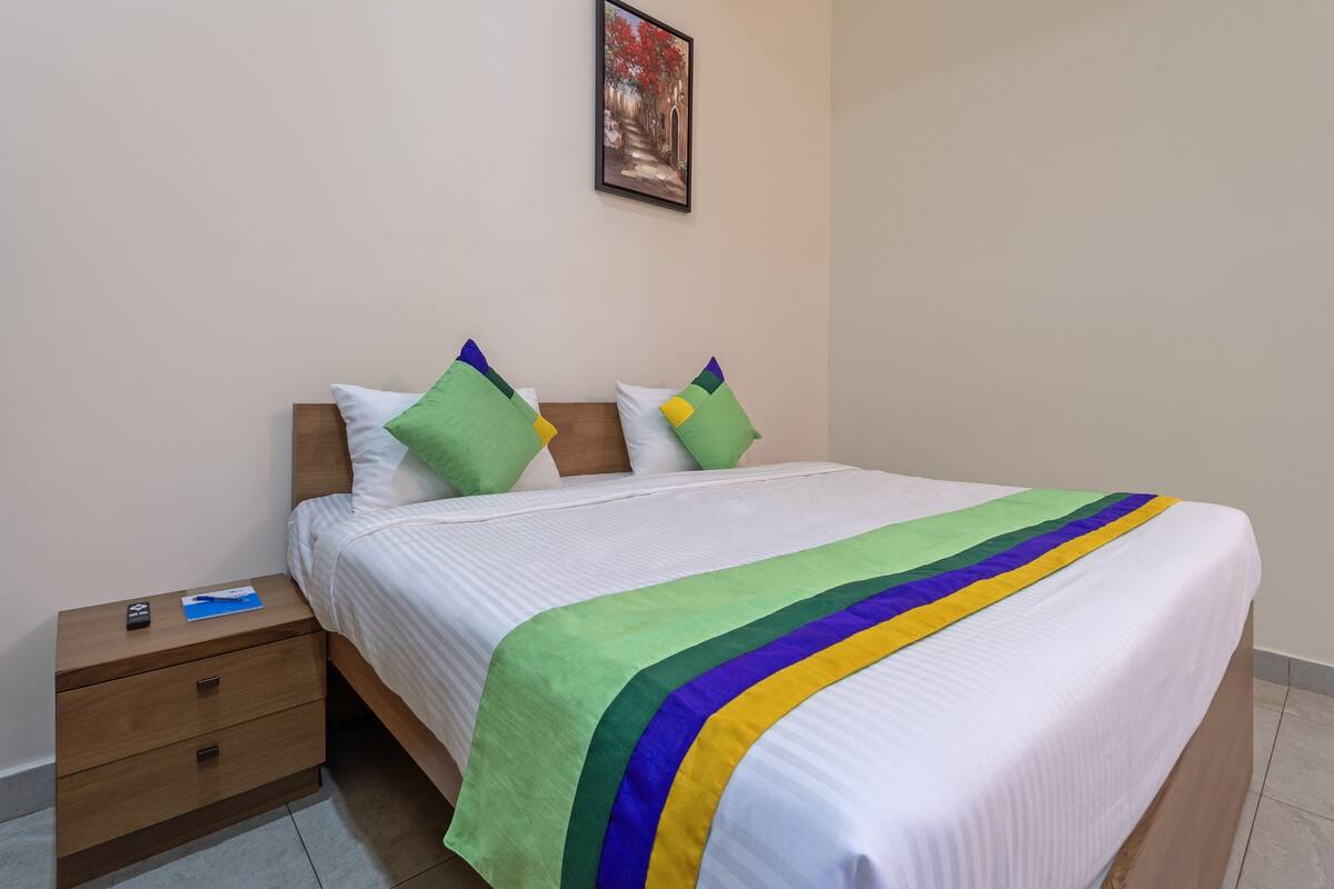 A neatly made bed with a striped bedspread, two pillows, and a wooden nightstand with a drawer.