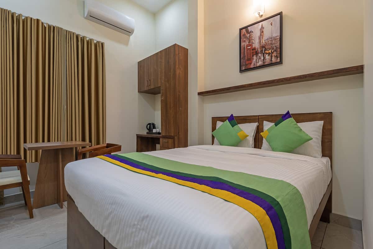 A hotel room with a bed, a desk, a chair, a wardrobe, and a painting on the wall.