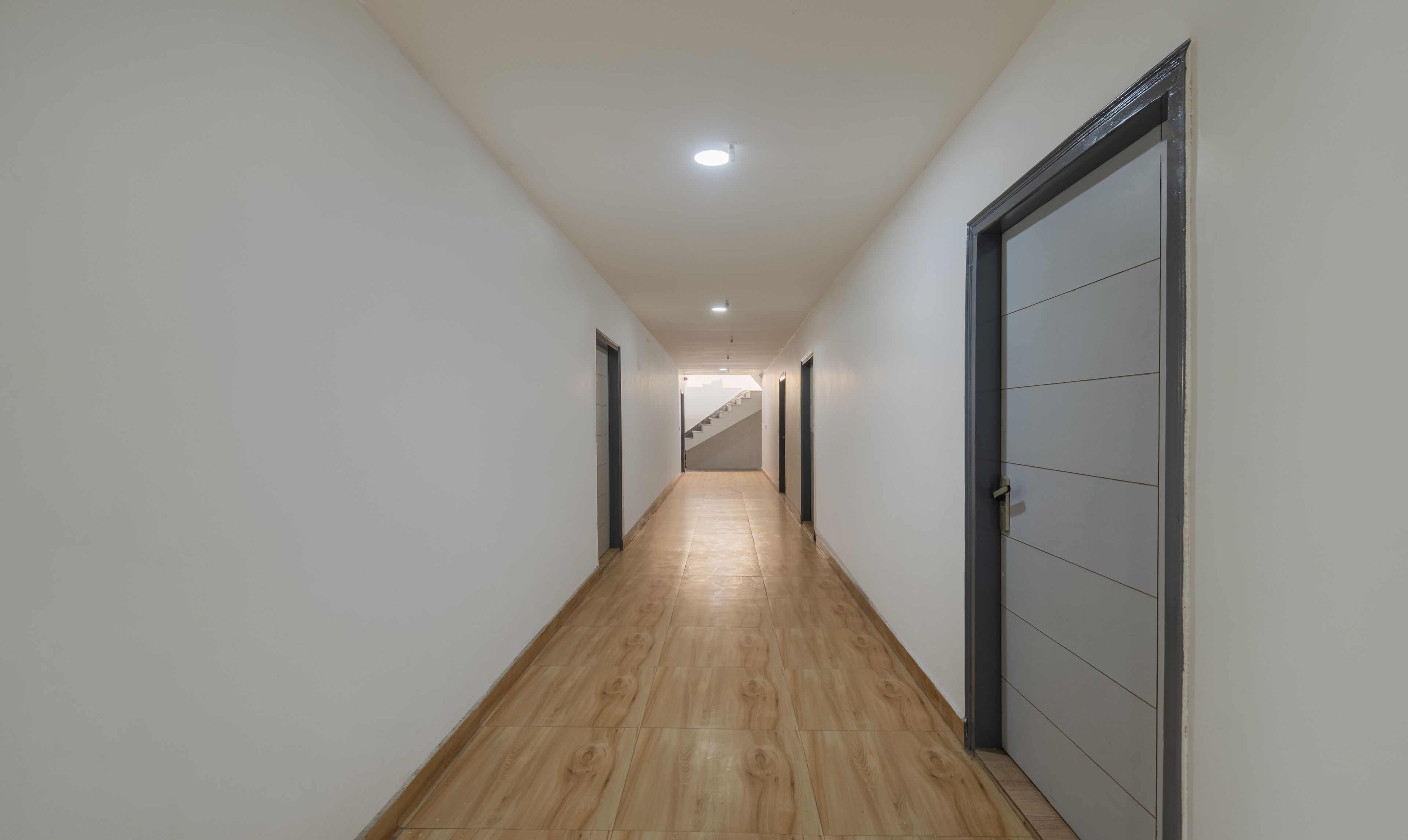 A hallway with wooden flooring, white walls, and a staircase at the end.