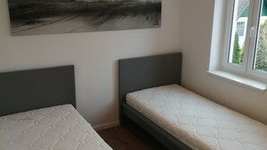 Une chambre avec deux lits simples, une grande peinture abstraite au mur et une fenêtre donnant sur un paysage verdoyant.