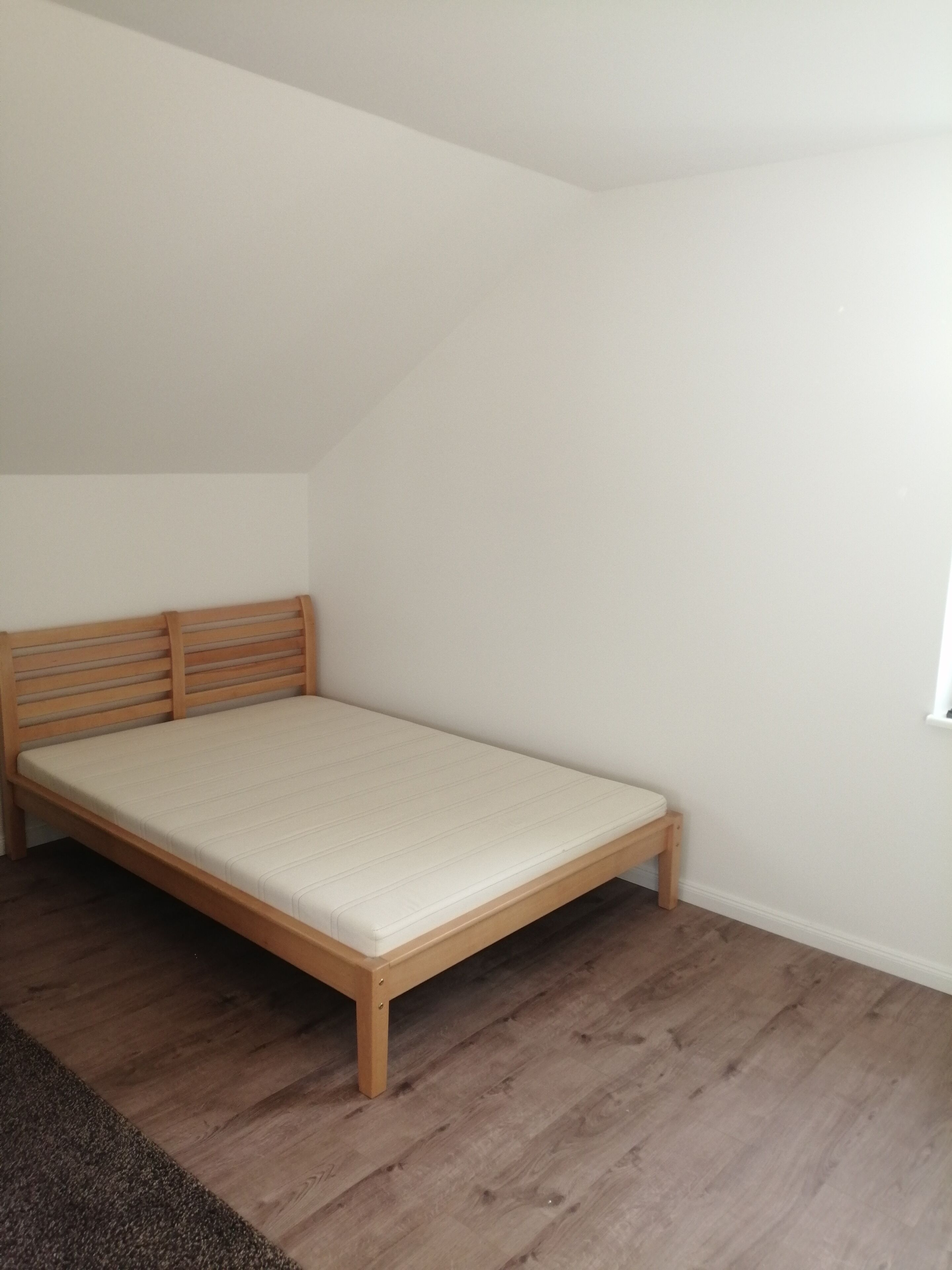 Una habitación pequeña con cama individual, techo inclinado y cabecera de madera.